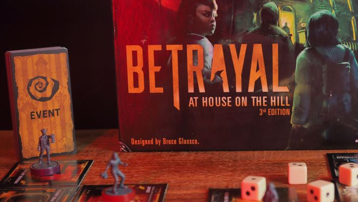 Betrayal at House on the Hill hộp, thẻ và token trên một bàn gỗ trước nền đen