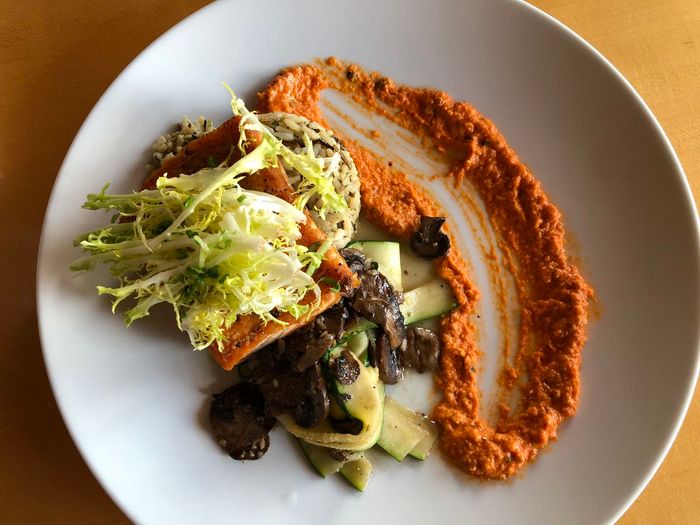 An overhead view of salmon accompanied by greens and a drizzle of orange sauce.