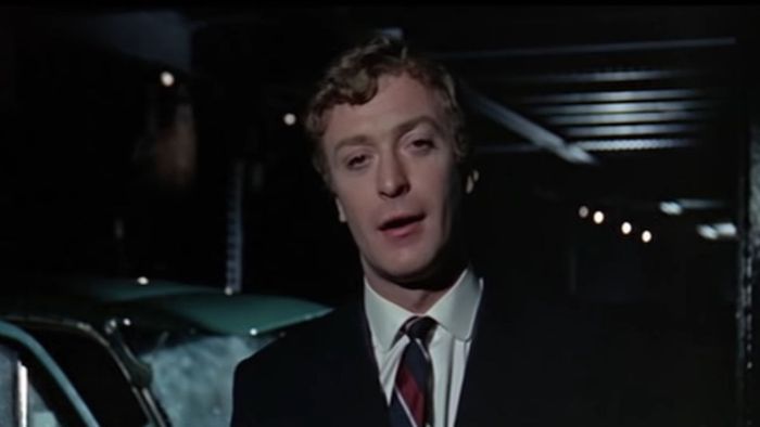 Michael Caine mặc bộ vest nói chuyện trước camera trong Alfie