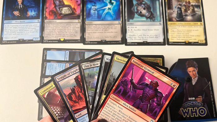 Một loạt các thẻ MTG Doctor Who được giơ lên phía trước, với một loạt các thẻ được sắp xếp trên một bàn ở phía sau