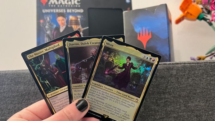 Ba lá bài từ Magic: The Gathering Doctor Who được giơ lên trước hộp Deck của Commander