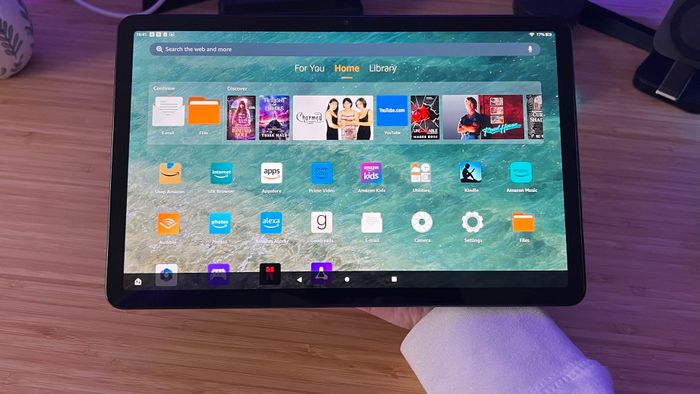 Amazon Fire Max 11 được cầm trên mặt sau của bàn làm việc gỗ