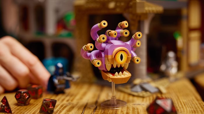 Beholder Lego trên một bàn được phủ bởi các viên xúc xắc, với một tay cầm minifigure gần đó