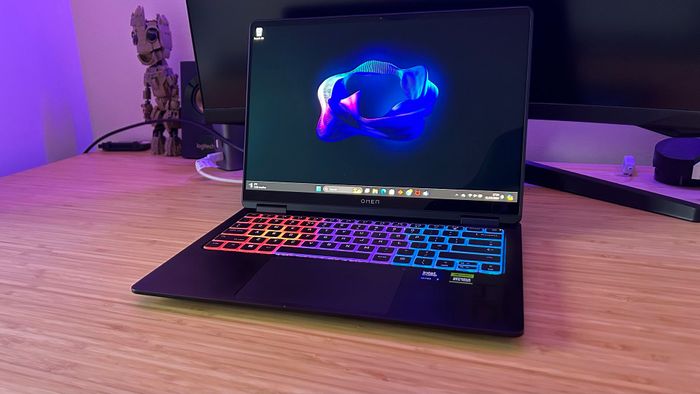 Laptop gaming HP Omen Transcend 14 đặt trên một bàn gỗ với một màn hình phía sau