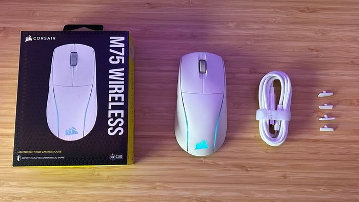 Corsair M75 Wireless với hộp, dây cáp và nút bên phụ bổ sung trên một bàn gỗ