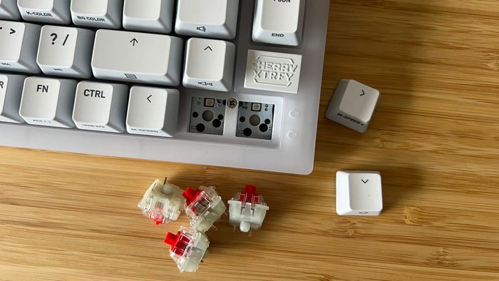 Góc của bàn phím Cherry XTRFY K5V2 với các switch và keycap được gỡ ra và đặt sang một bên trên một bàn gỗ