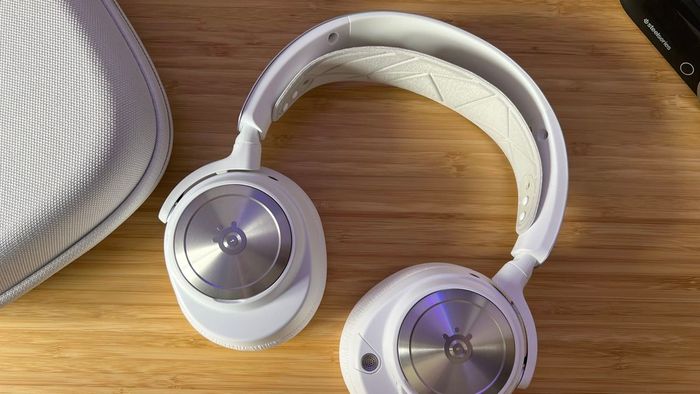 SteelSeries Arctis Nova Pro Wireless màu trắng nằm phẳng trên một bàn làm bằng gỗ