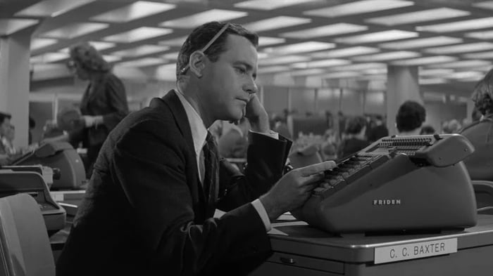 Jack Lemmon đóng vai một nhân viên văn phòng giết thời gian tại bàn làm việc của mình trong bộ phim Căn Hộ