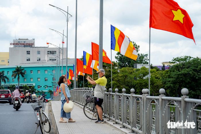 Du khách nước ngoài dừng lại trên cầu Phú Xuân để lưu lại khoảnh khắc và chụp bức ảnh với bảy đóa sen khổng lồ trên dòng sông Hương - Ảnh: LÊ ĐÌNH HOÀNG
