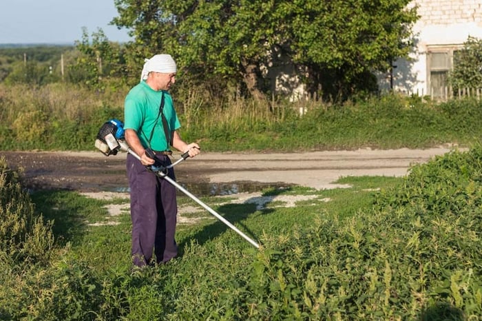 He is mowing the lawn using a machine