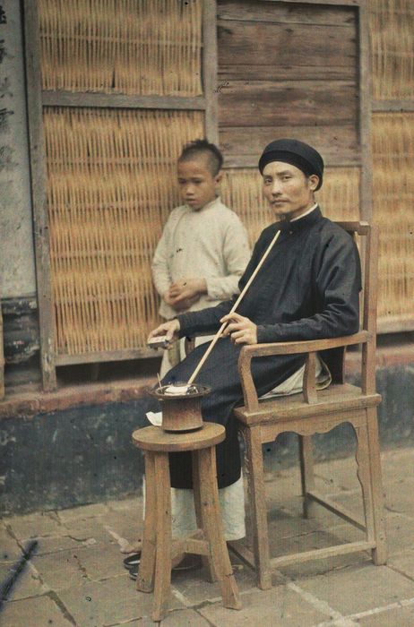 Một người đàn ông đang hút thuốc lào trên sân nhà - Ảnh: Léon Busy