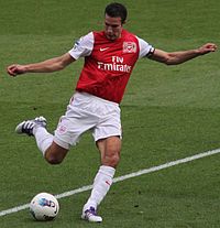 Robin van Persie, mặc áo bóng đá đỏ trắng và quần đùi trắng, chuẩn bị sút bóng bằng chân phải với hai tay dang rộng.