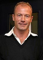 Alan Shearer mặc áo len đen với cổ áo trắng lộ ra.