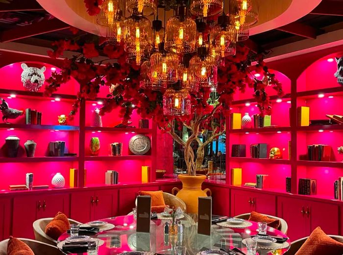 A vibrant pink dining space adorned with shelves, a grand chandelier, and floral decorations.