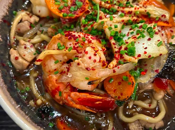 A hearty bowl brimming with shrimp, noodles, and a variety of flavorful toppings in a savory broth.