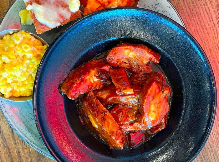 A top-down view of a bowl of rib tips surrounded by various side dishes.