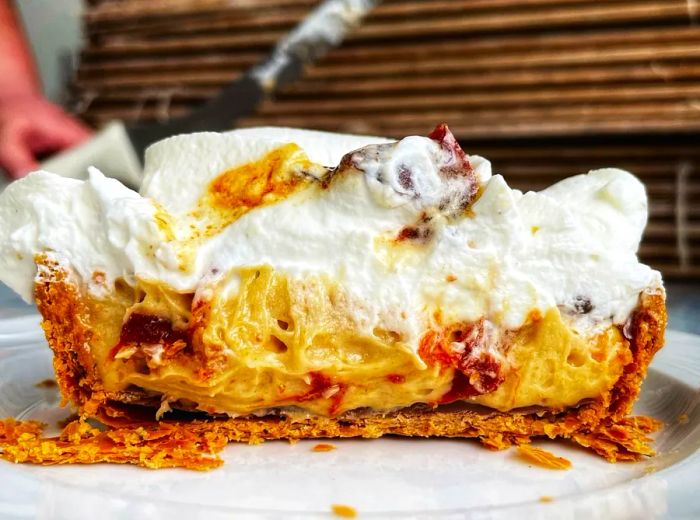 A slice of pie showcasing a gooey peanut butter center, rich whipped cream, a crumbly crust, and a sprinkle of toppings, all served on a plate.