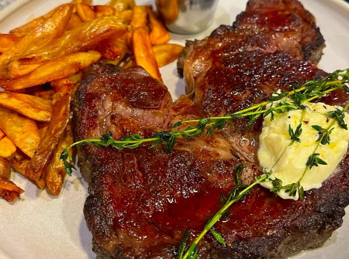 A juicy steak garnished with butter and herbs, accompanied by crispy French fries.