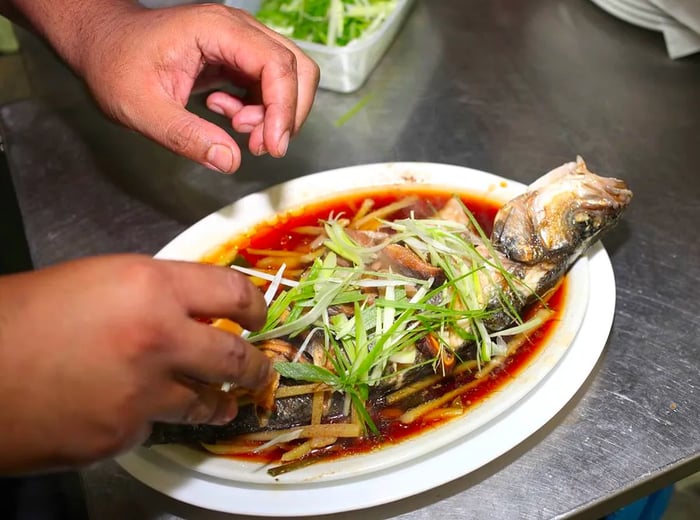 A chef garnishes a whole fish dish with fresh ingredients.