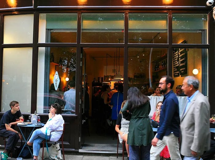 A crowd gathers outside a restaurant with expansive windows.