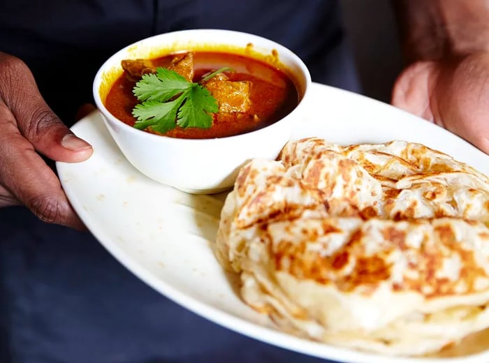 A server presents a tray of roti and dal.