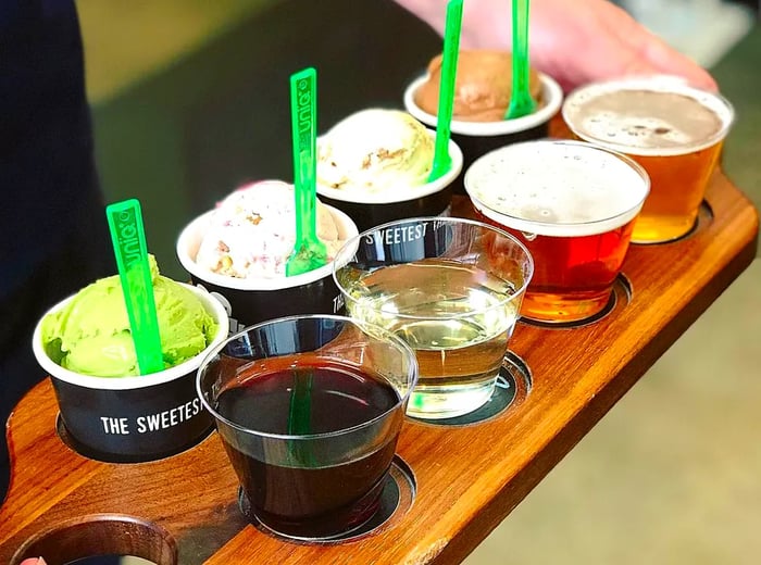 A server presents a wooden board filled with scoops of ice cream, alongside glasses of various drinks nestled in their own spaces.