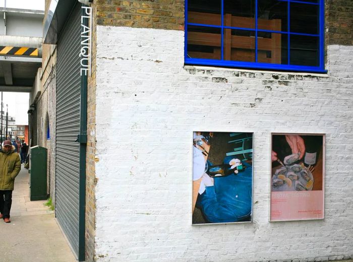 An exterior view of the restaurant showcasing artwork on a white brick wall and a small sign with its name.