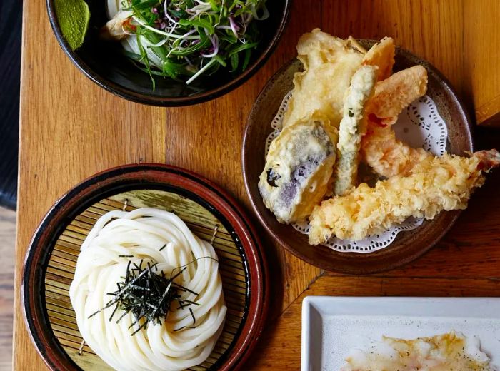 An overhead view of plates filled with noodles, tempura, and rice.