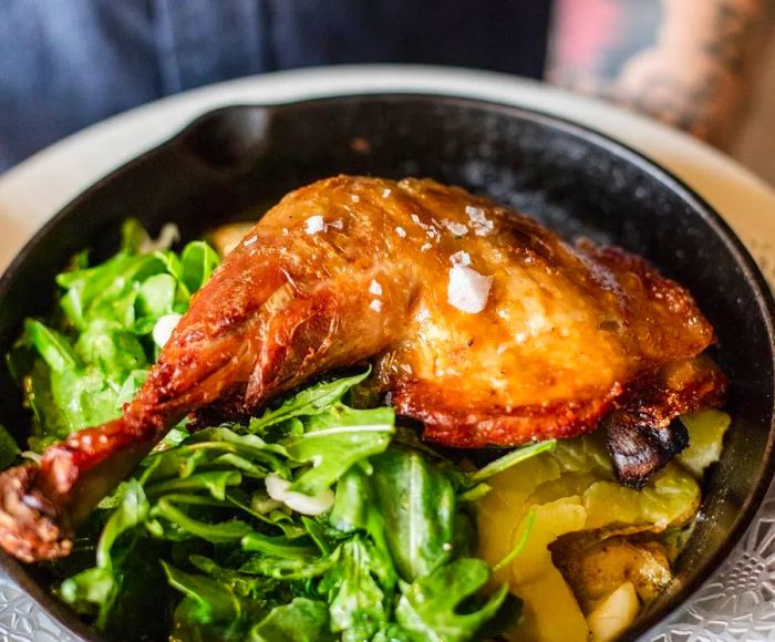 A succulent roasted chicken leg nestled in a cast iron skillet, surrounded by a vibrant mix of greens and vegetables.