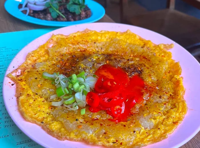 A vibrant pink plate featuring noodles fried into a crisp sheet, adorned with sliced vegetables.