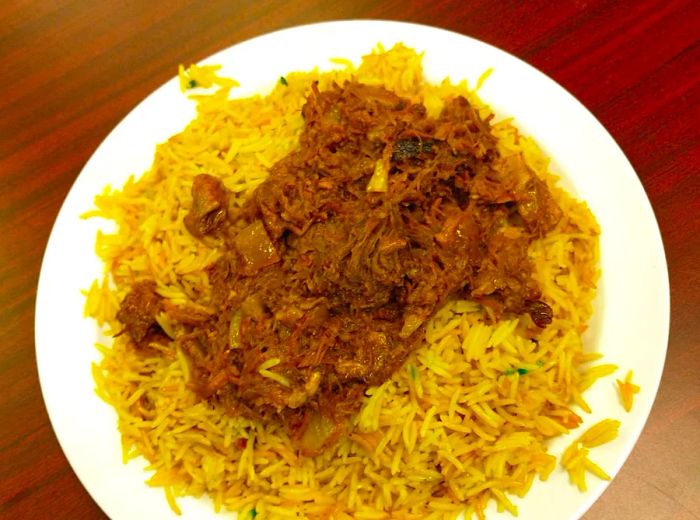 A dish featuring tender goat meat served over a bed of yellow rice.