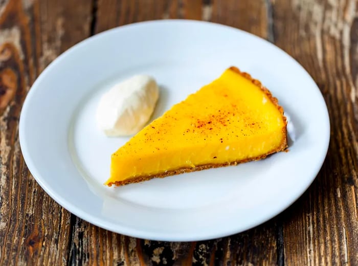 A single slice of lemon tart accompanied by a dollop of cream.