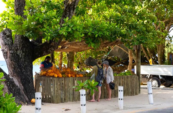 Tourists walk barefoot as they explore a coconut water stand by the beach.