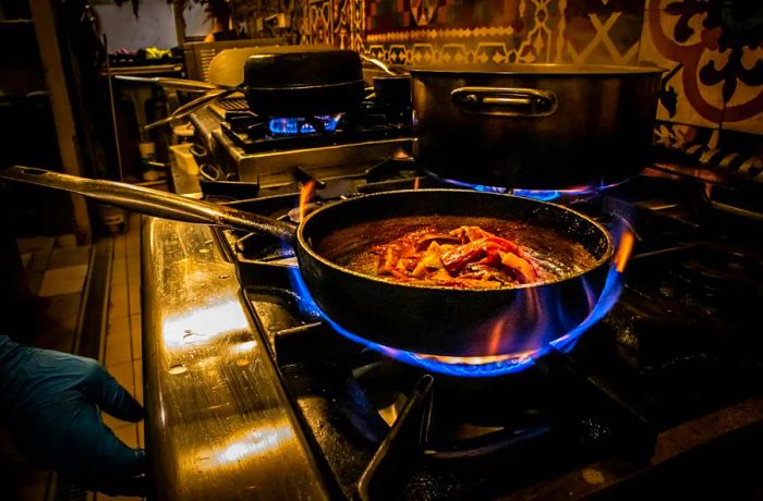 A sizzling pan of food being prepared over a flame in a restaurant kitchen.