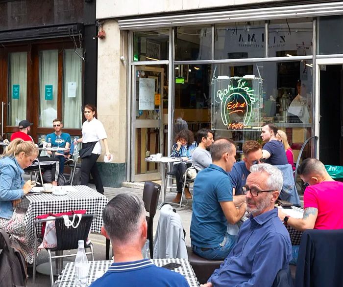 Patrons enjoying their time on the outdoor terrace of a restaurant with a neon sign reading Bar Italia.