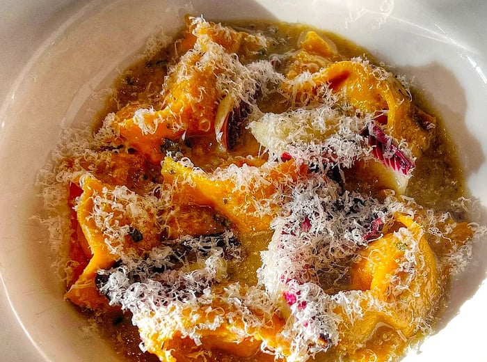 A plate of agnolotti, bathed in the warm glow of autumn, topped with Parmesan and vibrant purple radicchio leaves.