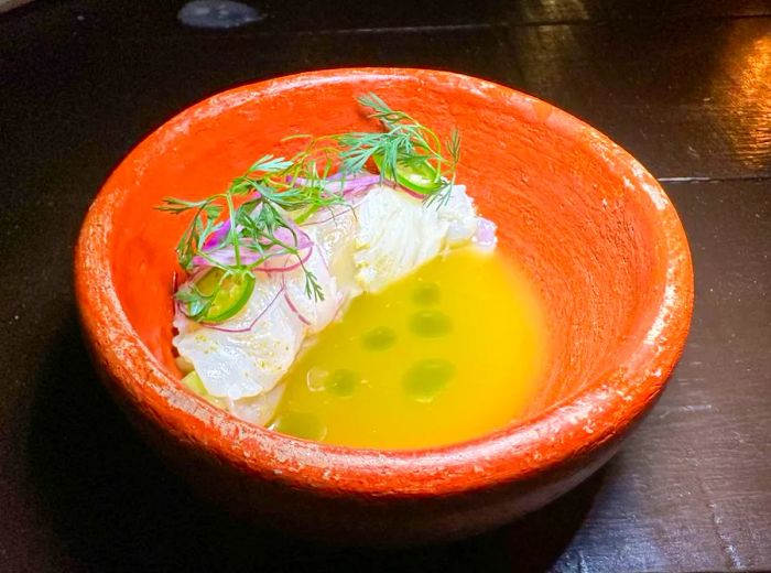 A clay bowl filled with ceviche, showcasing slices of fish arranged around the rim of a vibrant yellow broth.