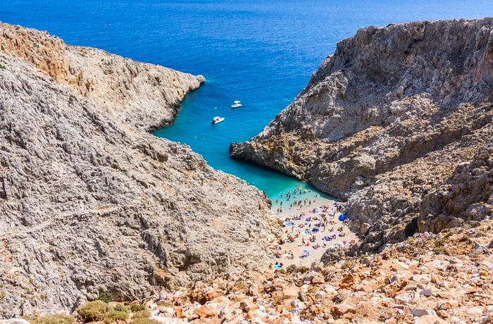 A distant view captures beachgoers relaxing on a sandy shore nestled between two rugged mountains.