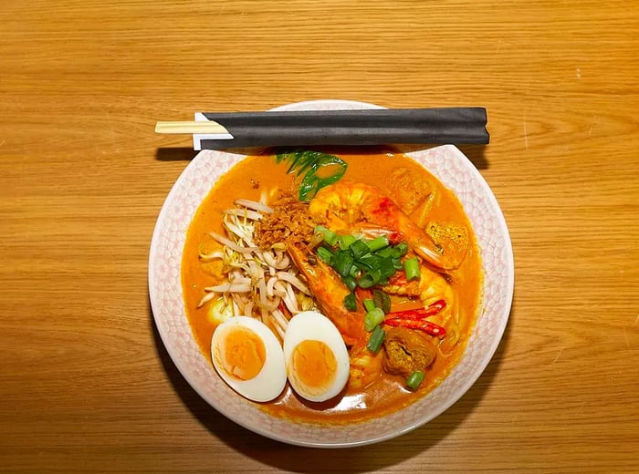 A generous bowl of curry laksa, with eggs and vegetables peeking through the rich broth, accompanied by chopsticks resting on the edge.