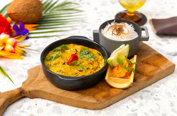 A pot of curry with a red pepper garnish, next to a handled pot filled with rice and sides.