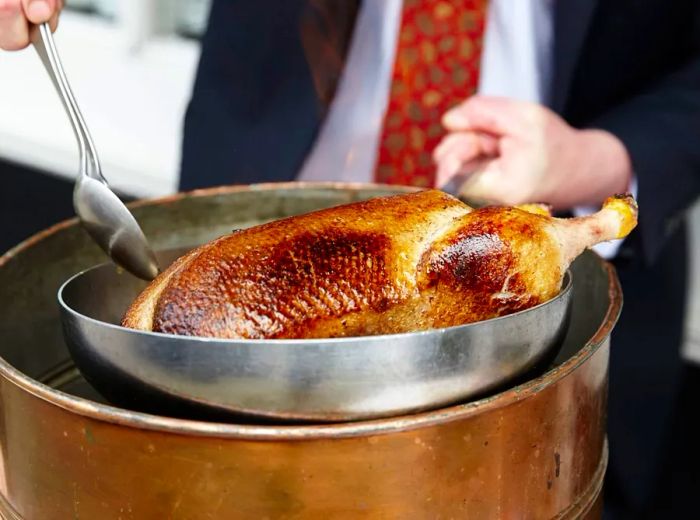 A chef extracts a duck from a gleaming brass pot.