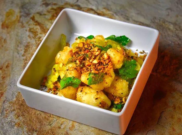 A square dish brimming with vibrant yellow cauliflower, garnished with a sprinkle of chopped nuts and fresh herbs.