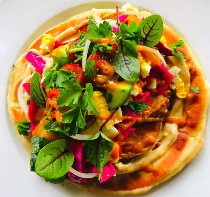 A flatbread adorned with a vibrant mix of vegetables, viewed from above.