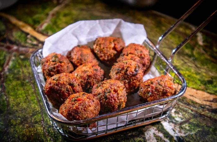 A basket of meatballs frying in hot oil.