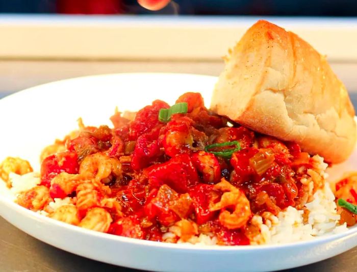 A chef garnishes a bowl of crawfish etouffee, paired with a generous piece of bread.