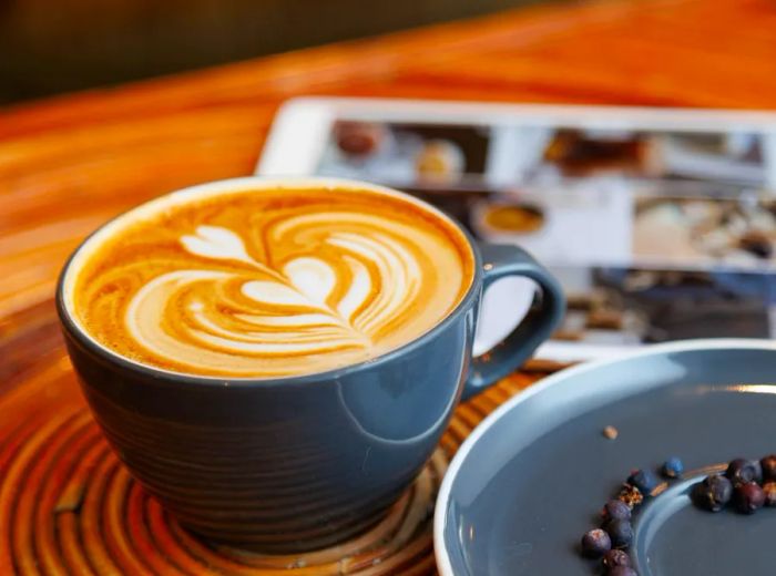 A latte adorned with intricate foam art, resting on a mat next to a selection of coffee beans.