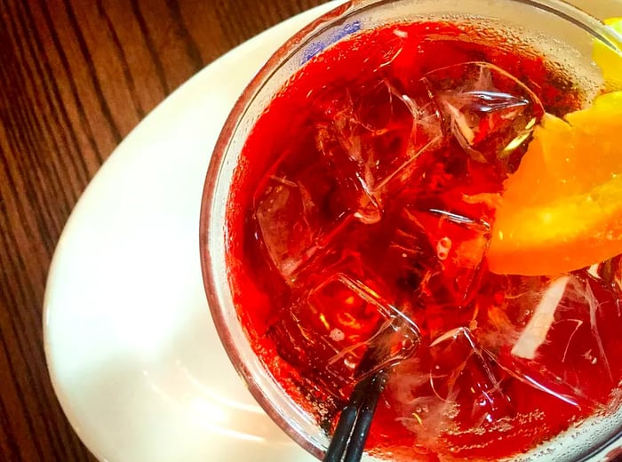 A striking deep red cocktail garnished with an orange wedge, seen from above.