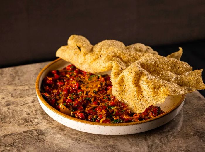 A plate of beef tartare garnished with various accompaniments, topped with a crisp, wavy flatbread.