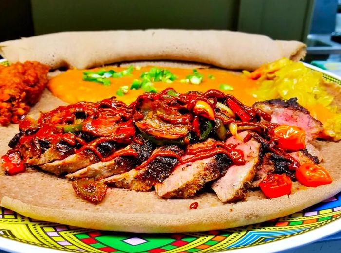 Tender slices of steak nestled under roasted vegetables and awaze sauce, served on a bed of injera accompanied by an assortment of sides.