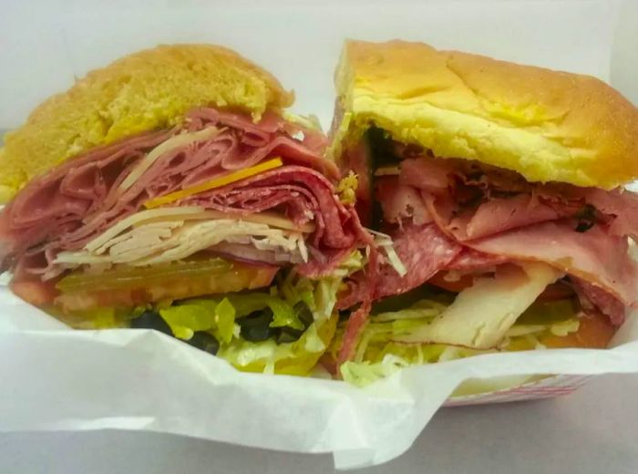 A sandwich cut in half and nestled in a takeout container, featuring generous layers of sliced beef and turkey, cheese, lettuce, and tomato.